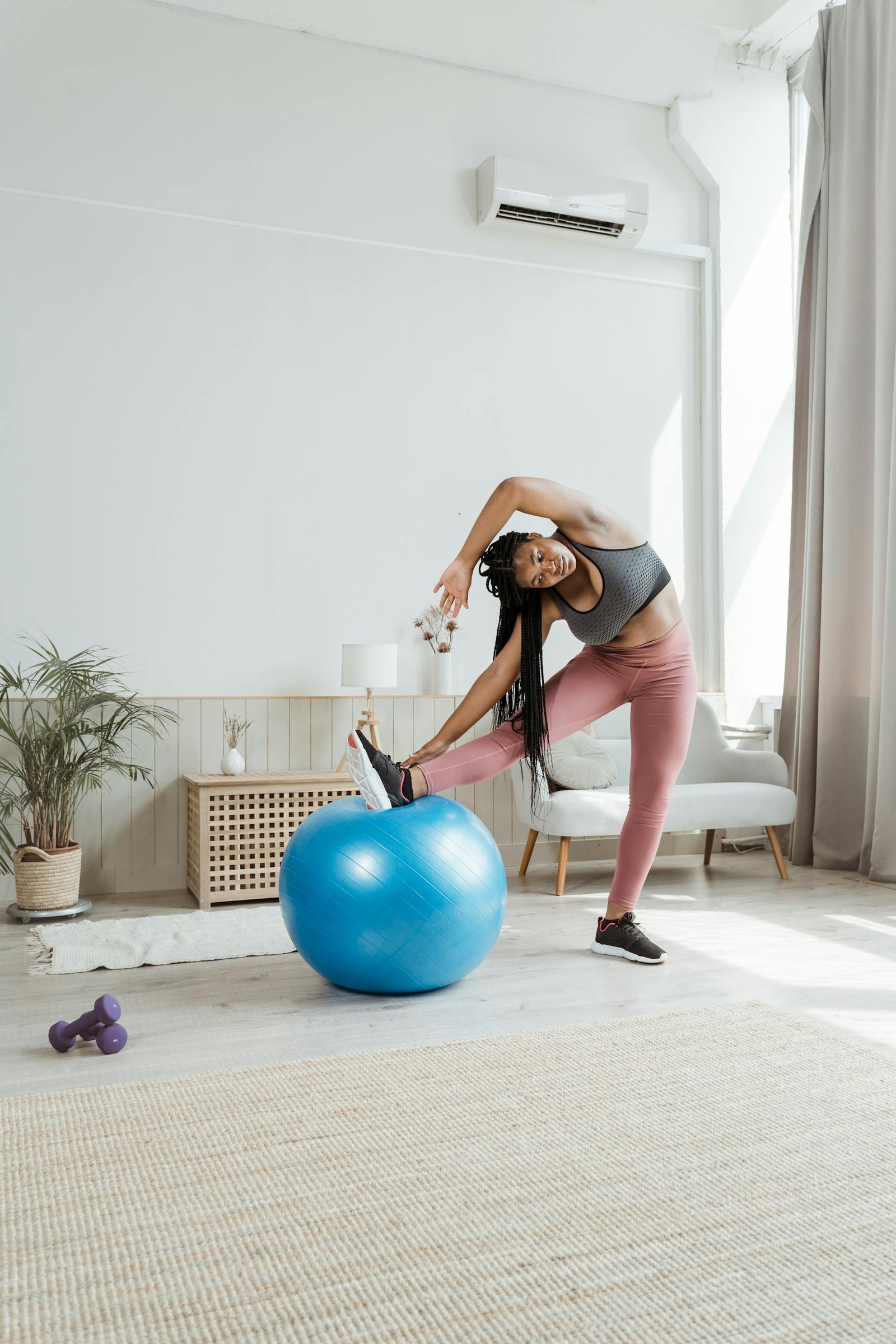 A woman in activewear stretches with a yoga ball in a bright and airy living room.